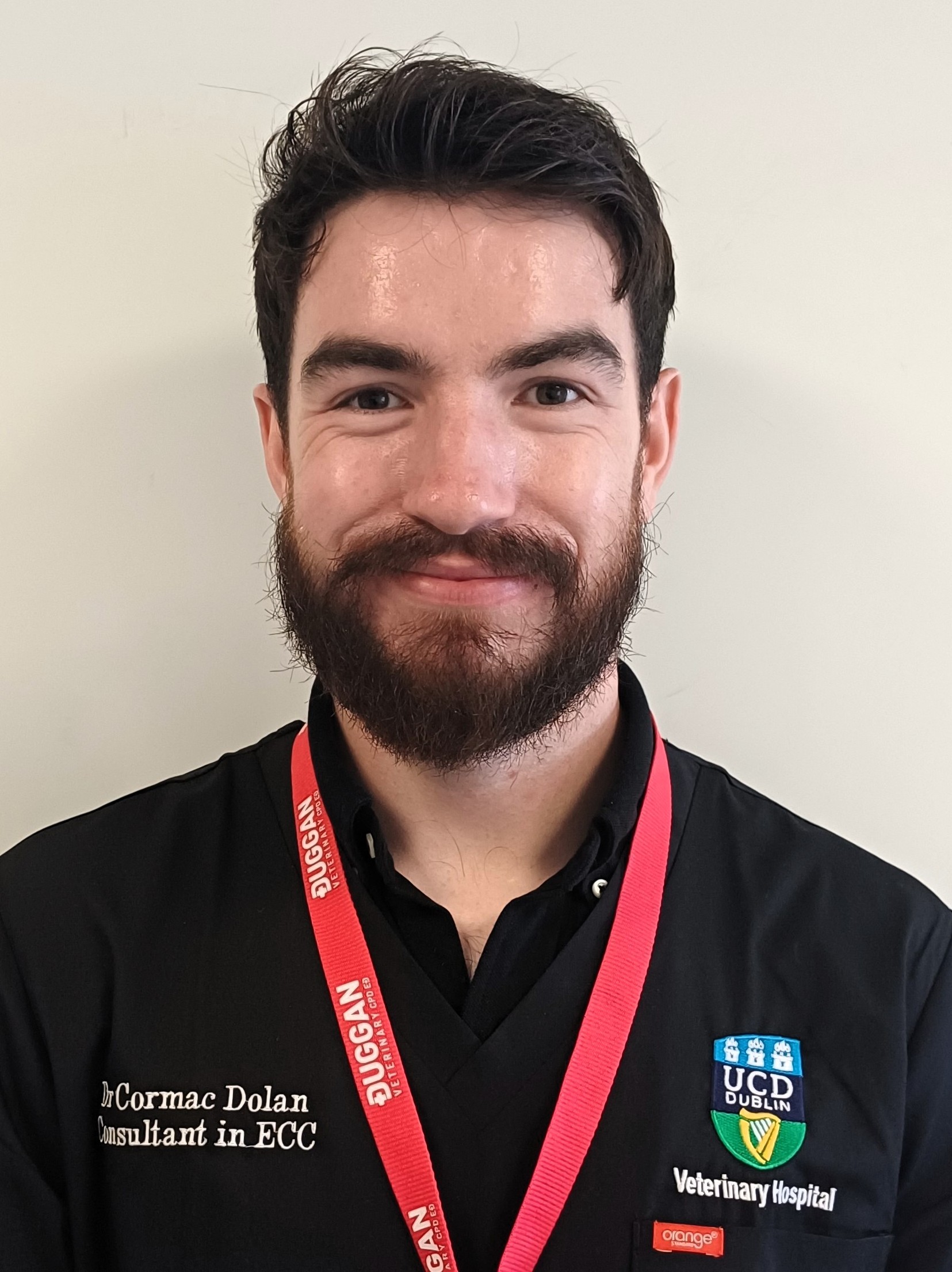 Cormac Dolan smiles while wearing navy scrubs and a pink lanyard